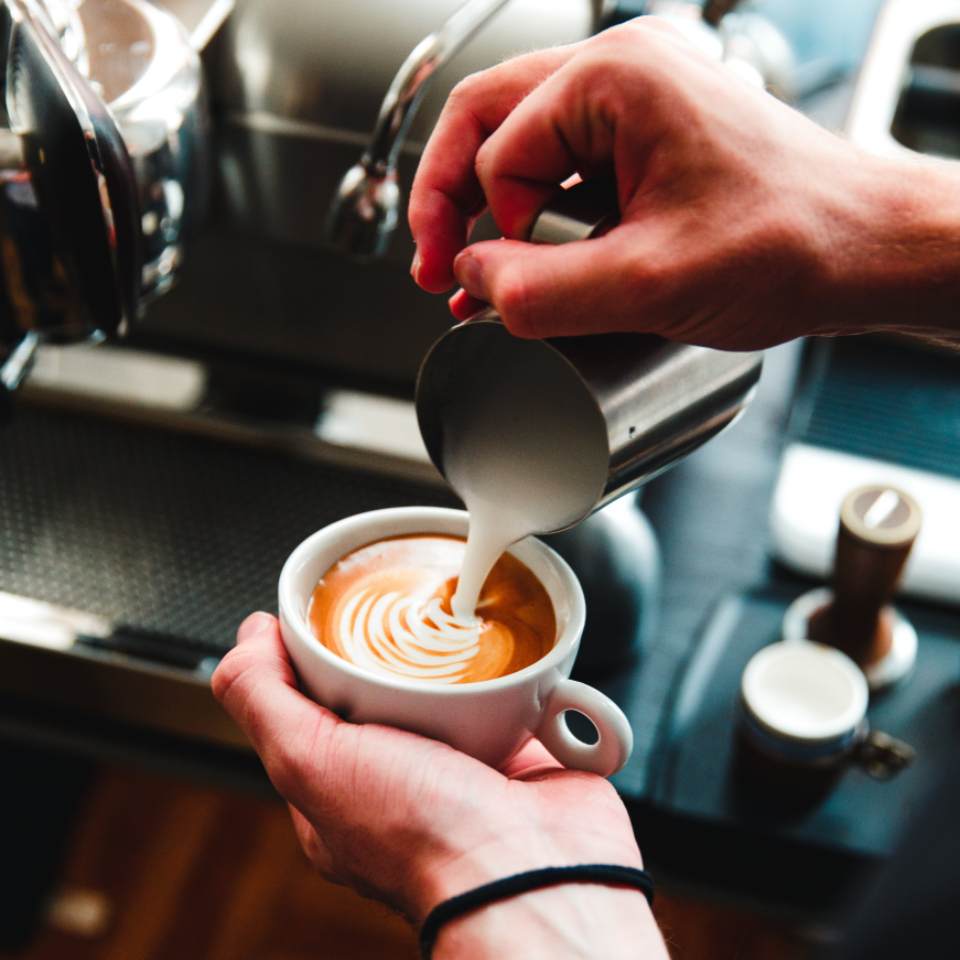 Barista pouring latte art into a ceramic cup at the espresso bar